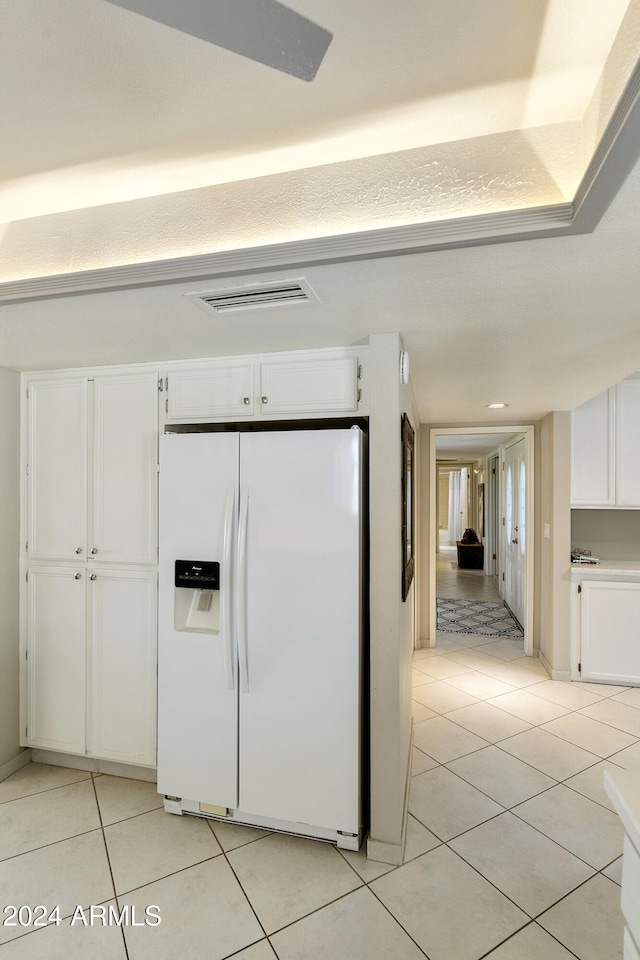 kitchen with white refrigerator with ice dispenser, light tile patterned floors, and white cabinetry