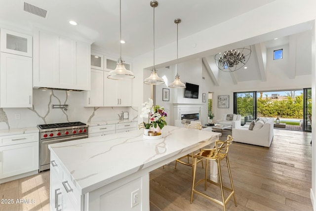 kitchen with designer range, white cabinets, a glass covered fireplace, open floor plan, and backsplash