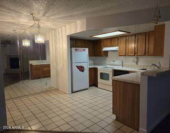 kitchen featuring pendant lighting, sink, white appliances, a textured ceiling, and tile counters