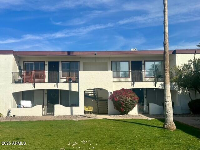 rear view of house featuring a yard, a balcony, and stucco siding