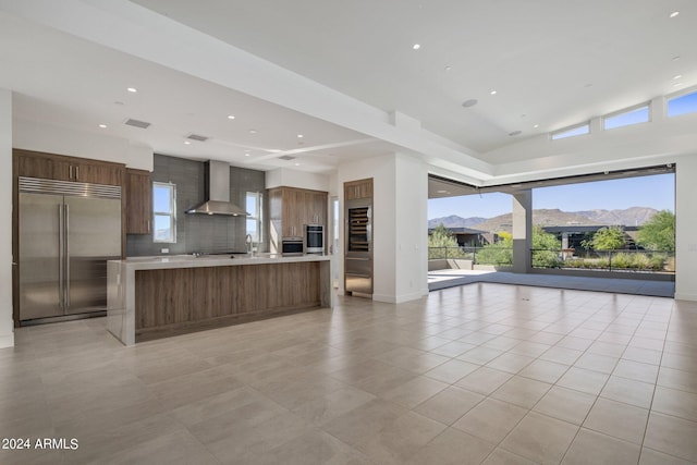 kitchen with tasteful backsplash, stainless steel appliances, wall chimney range hood, a mountain view, and a kitchen island