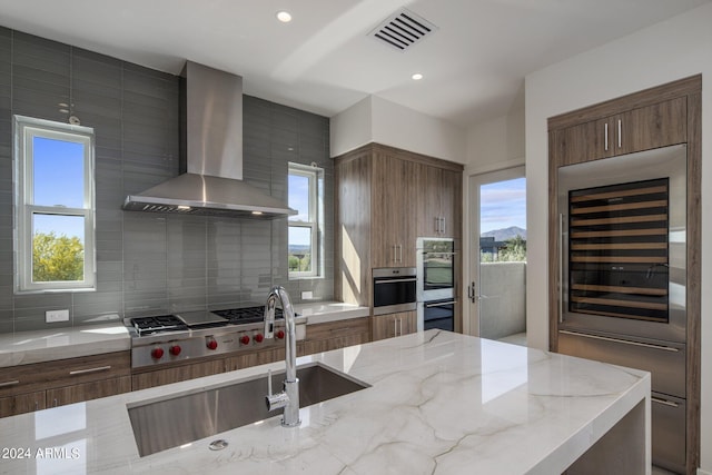 kitchen with backsplash, beverage cooler, wall chimney exhaust hood, light stone countertops, and stainless steel gas cooktop