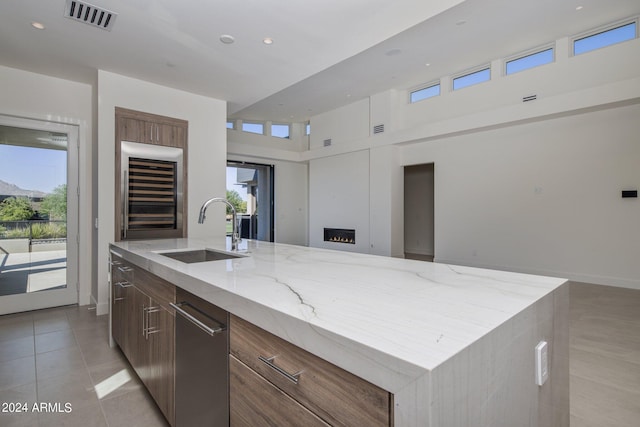 kitchen featuring sink, wine cooler, light stone countertops, light tile patterned floors, and an island with sink