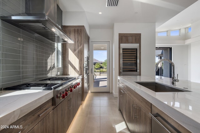 kitchen with sink, beverage cooler, wall chimney range hood, light tile patterned floors, and appliances with stainless steel finishes