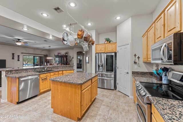 kitchen featuring ceiling fan with notable chandelier, appliances with stainless steel finishes, a center island, and sink