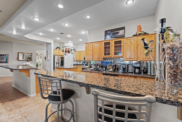 kitchen featuring light tile patterned floors, stainless steel fridge with ice dispenser, a center island, dark stone countertops, and a breakfast bar area