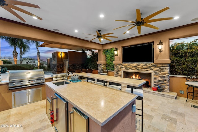 kitchen featuring an island with sink, an outdoor stone fireplace, stainless steel refrigerator, crown molding, and ceiling fan