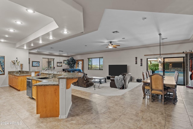 kitchen with ceiling fan, a raised ceiling, hanging light fixtures, sink, and a spacious island