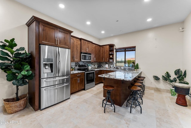 kitchen with kitchen peninsula, tasteful backsplash, appliances with stainless steel finishes, a breakfast bar, and light stone countertops