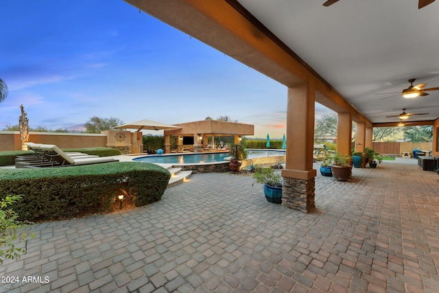 patio terrace at dusk with a fenced in pool and ceiling fan