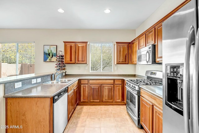 kitchen with brown cabinetry, appliances with stainless steel finishes, a peninsula, and a sink