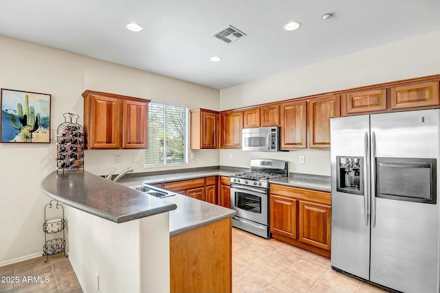 kitchen with visible vents, a sink, stainless steel appliances, a peninsula, and brown cabinetry