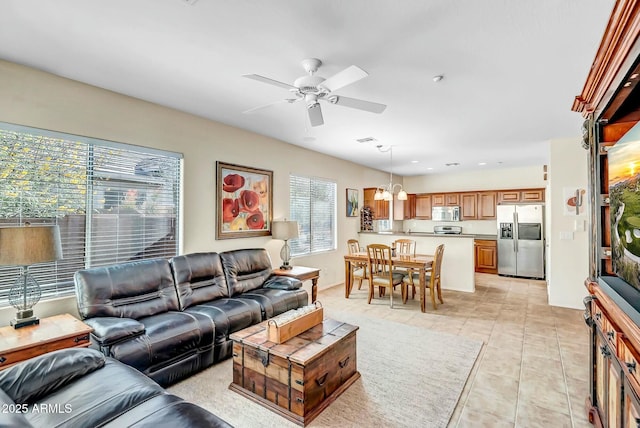 living area with light tile patterned floors, visible vents, and ceiling fan with notable chandelier