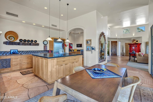 kitchen featuring a towering ceiling, decorative light fixtures, and light brown cabinets