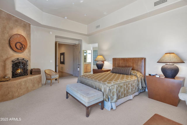 carpeted bedroom featuring a large fireplace and a tray ceiling