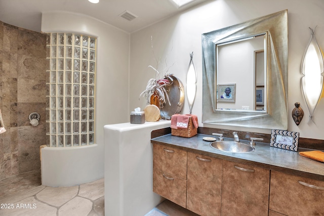 bathroom with tiled shower and vanity