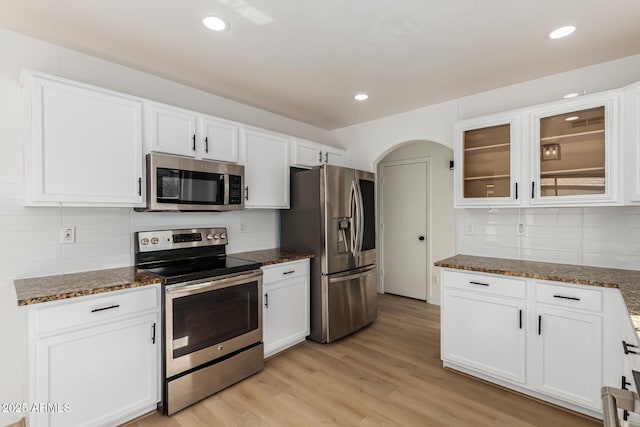 2112 S 160th Dr, Goodyear, AZ 85338 - kitchen with stainless steel appliances, tasteful backsplash, white cabinets, dark stone counters, and glass insert cabinets