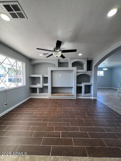 unfurnished living room featuring ceiling fan, built in shelves, and a textured ceiling