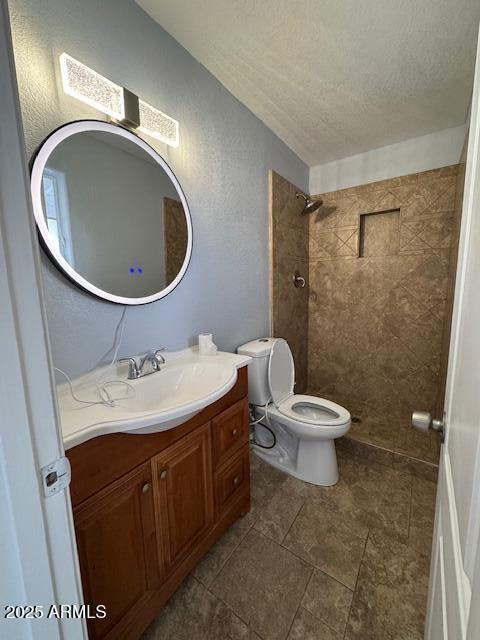 bathroom featuring a textured ceiling, toilet, vanity, and a tile shower