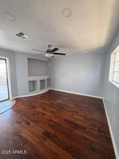 unfurnished living room featuring ceiling fan, built in shelves, and dark hardwood / wood-style flooring