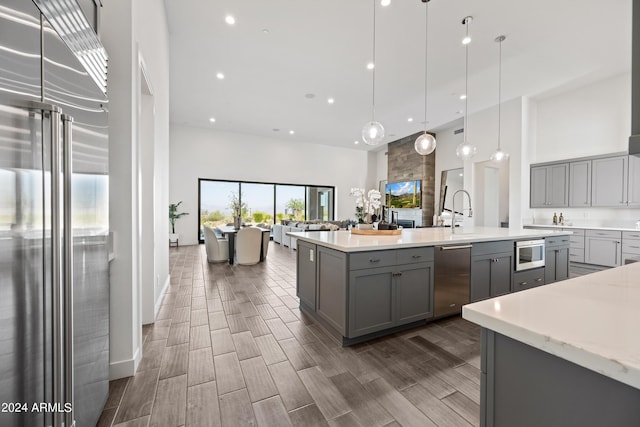 kitchen with gray cabinets, appliances with stainless steel finishes, a towering ceiling, and decorative light fixtures