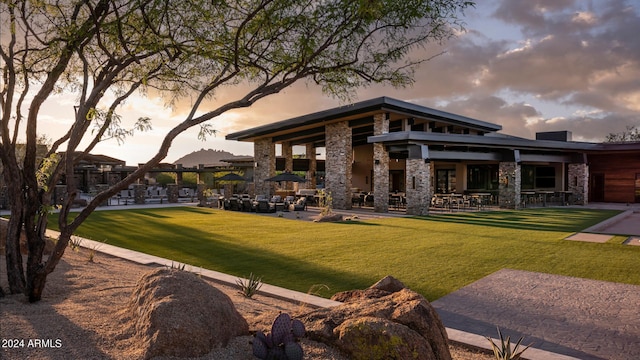 back house at dusk with a patio area and a lawn