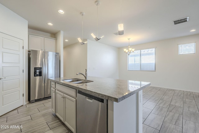 kitchen with sink, stainless steel appliances, an inviting chandelier, an island with sink, and pendant lighting