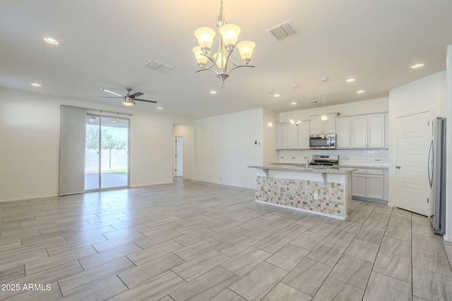 kitchen featuring a center island with sink, ceiling fan with notable chandelier, white cabinets, hanging light fixtures, and stainless steel appliances