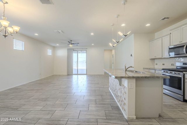 kitchen featuring ceiling fan with notable chandelier, stainless steel appliances, a kitchen island with sink, sink, and hanging light fixtures