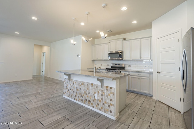 kitchen with white cabinets, hanging light fixtures, stainless steel appliances, and a kitchen island with sink