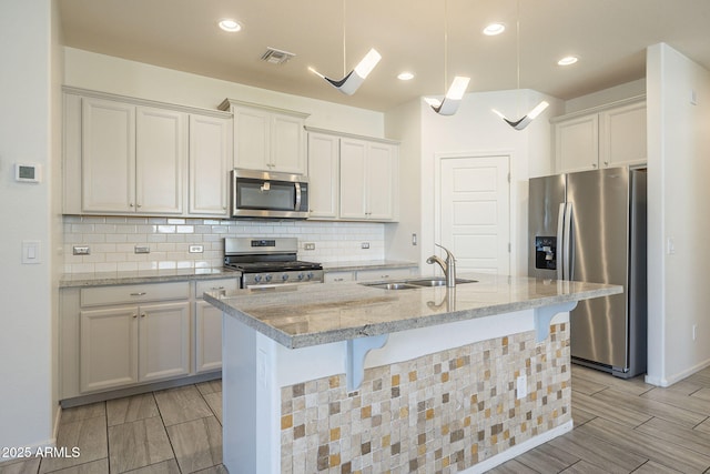 kitchen with light stone countertops, sink, a center island with sink, and appliances with stainless steel finishes