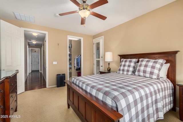 carpeted bedroom featuring a walk in closet, a closet, and ceiling fan