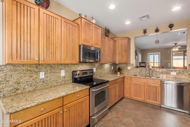 kitchen featuring appliances with stainless steel finishes, light stone countertops, ceiling fan, sink, and tasteful backsplash