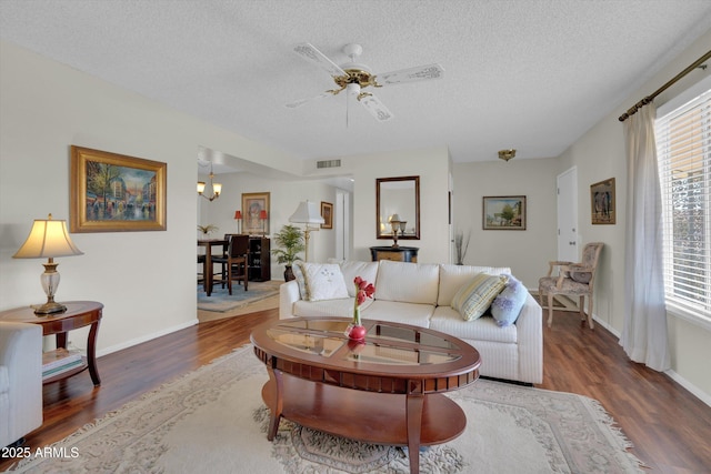 living room featuring ceiling fan with notable chandelier, dark wood-type flooring, and a textured ceiling