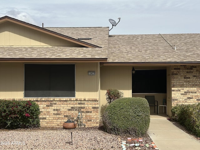 doorway to property featuring brick siding and a shingled roof