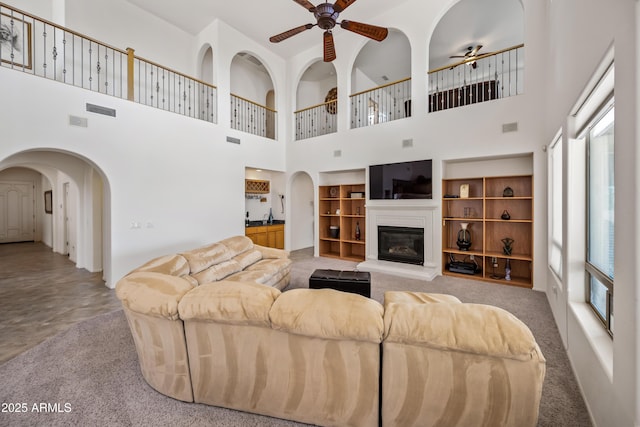 19242 W Pasadena Ave, Litchfield Park, AZ 85340 - living room with ceiling fan, carpet, arched walkways, a towering ceiling, and a glass covered fireplace