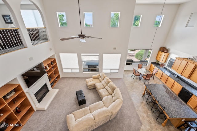 19242 W Pasadena Ave, Litchfield Park, AZ 85340 - living room featuring a high ceiling, plenty of natural light, a glass covered fireplace, ceiling fan, and light carpet