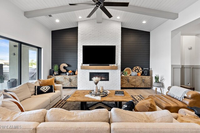 living room featuring a fireplace, wood walls, beamed ceiling, and light wood-type flooring