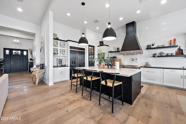 kitchen featuring white cabinetry, wall chimney exhaust hood, a center island with sink, and built in refrigerator