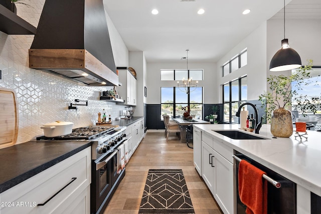 kitchen with stainless steel appliances, wall chimney range hood, sink, and pendant lighting