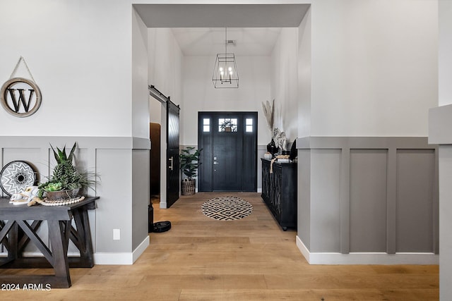 entryway with a towering ceiling, an inviting chandelier, a barn door, and light hardwood / wood-style floors