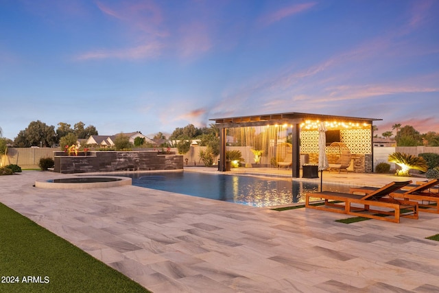 pool at dusk with an in ground hot tub, a patio area, pool water feature, and a gazebo