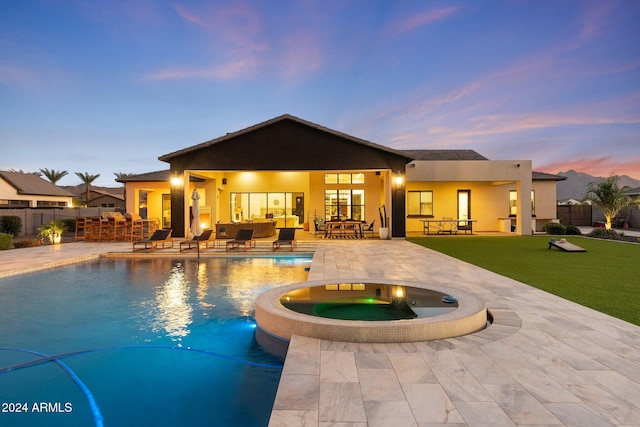 pool at dusk featuring an in ground hot tub, a patio, a yard, and outdoor lounge area