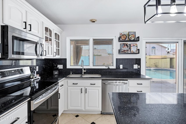 kitchen with glass insert cabinets, dark stone counters, white cabinetry, a sink, and stainless steel appliances