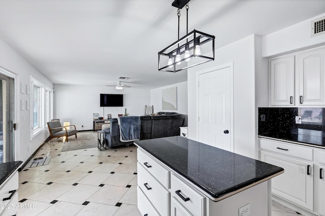 kitchen with a ceiling fan, decorative light fixtures, a center island, dark stone counters, and white cabinetry
