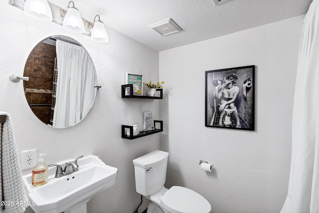 bathroom featuring a textured ceiling, visible vents, a sink, toilet, and a textured wall