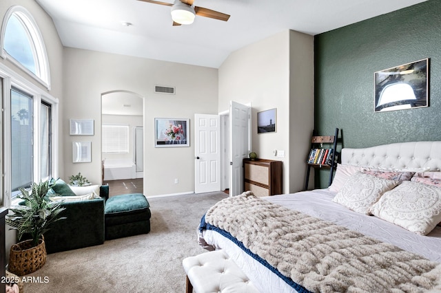 carpeted bedroom featuring visible vents, arched walkways, high vaulted ceiling, baseboards, and ensuite bath