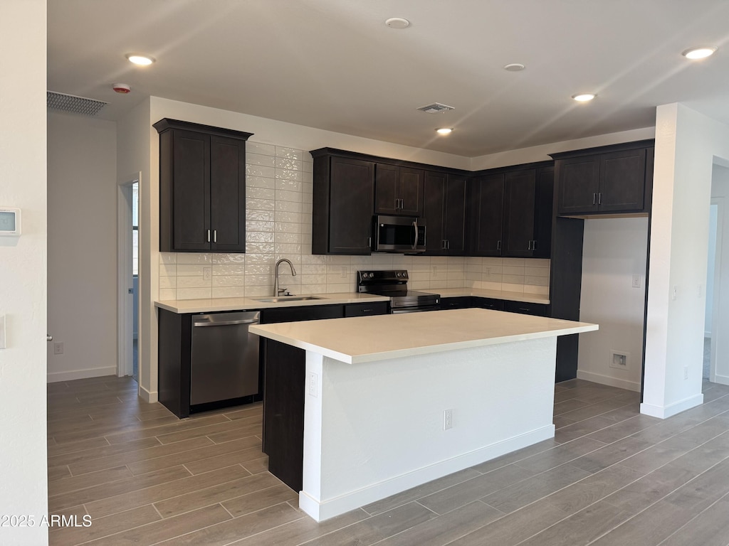 kitchen featuring light wood-type flooring, stainless steel appliances, a kitchen island, and sink