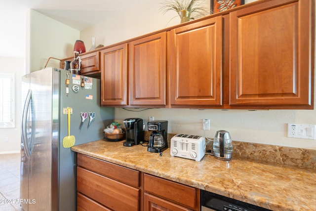 kitchen with light stone counters, stainless steel refrigerator, and tile patterned flooring