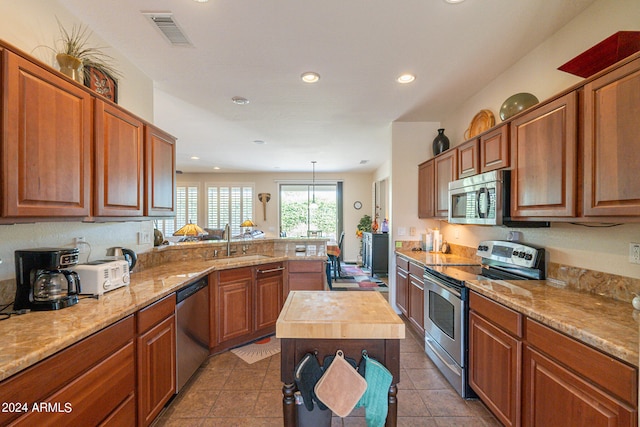 kitchen with sink, kitchen peninsula, a kitchen island, stainless steel appliances, and wood counters